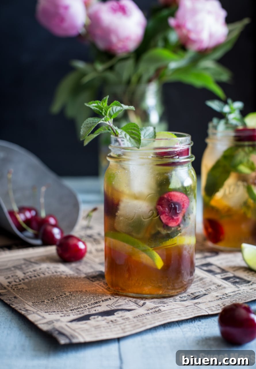 Hand holding a Black Cherry Mule in a mason jar, with a bowl of fresh cherries in the background.