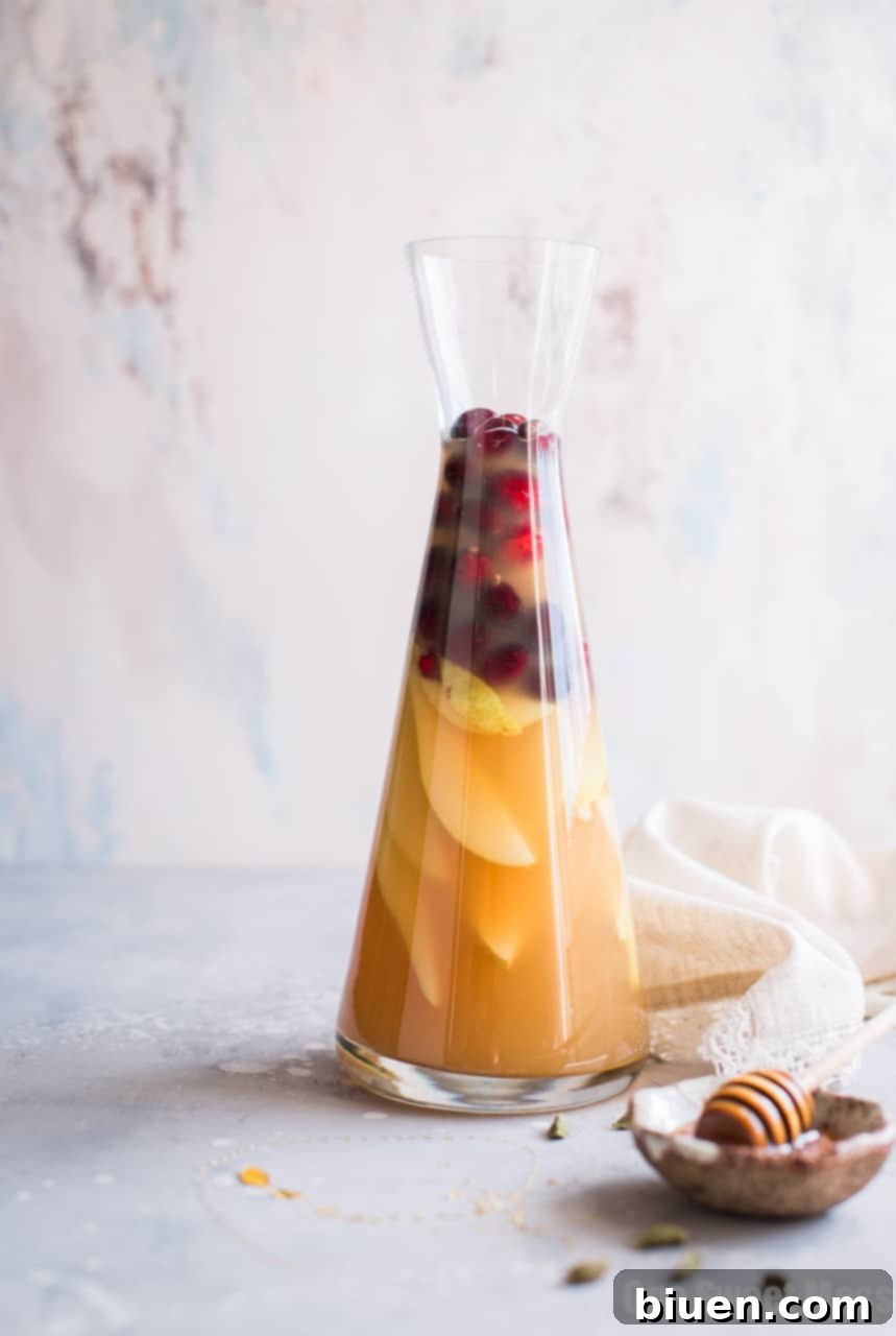 Close-up of Honey Pear Cardamom Sangria in a glass, garnished with pear slices and cranberries