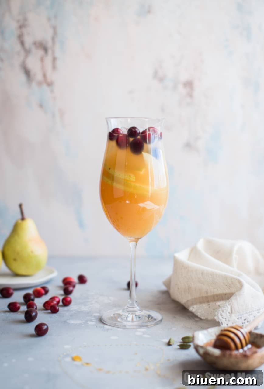 Pouring Honey Pear Cardamom Sangria into a glass with ice and fruit