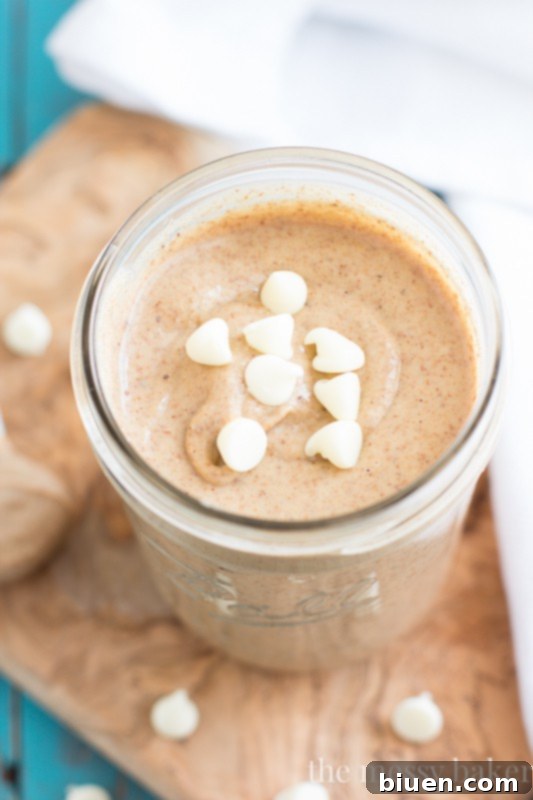 A jar of white chocolate cinnamon almond butter with a spoon, inviting you to indulge. Perfect for various sweet and savory applications.