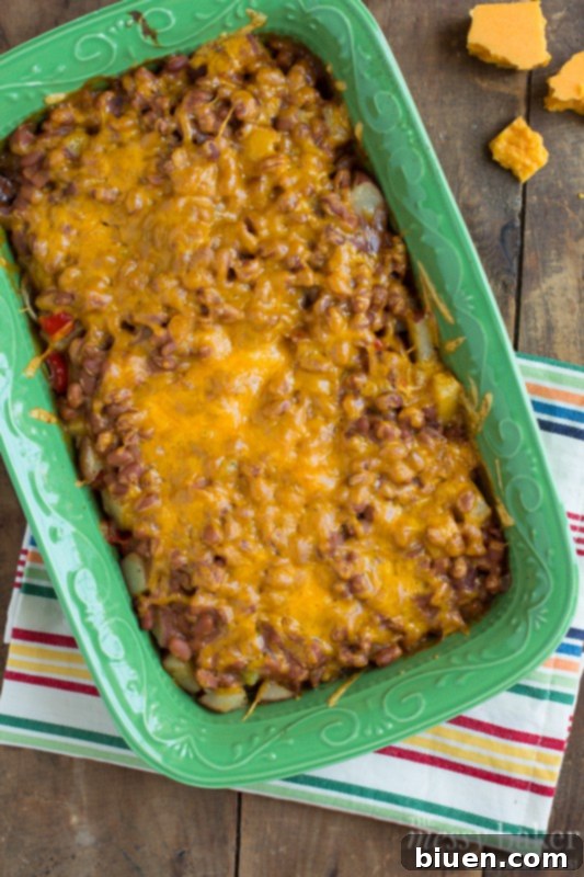 Casserole dish filled with layers of potato, beans, and cheese before baking