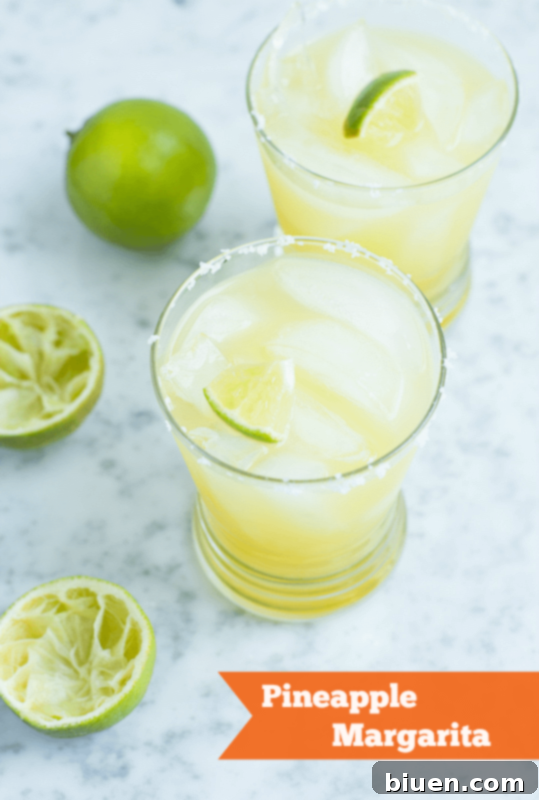 Fresh Pineapple Margarita in a tall glass with lime and pineapple garnish