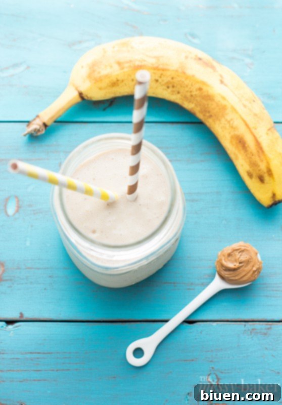 Wholesome PB Banana Oat Boost 3 Top-down view of a peanut butter banana oat smoothie in a glass with a spoon, highlighting its creamy texture and a banana slice garnish.