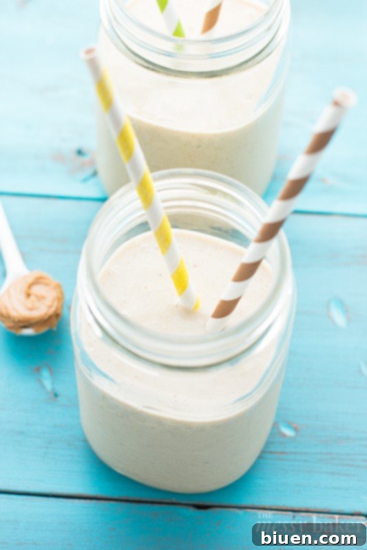 Wholesome PB Banana Oat Boost 4 A glass of peanut butter banana oat smoothie served on a rustic wooden board, emphasizing its thick consistency.