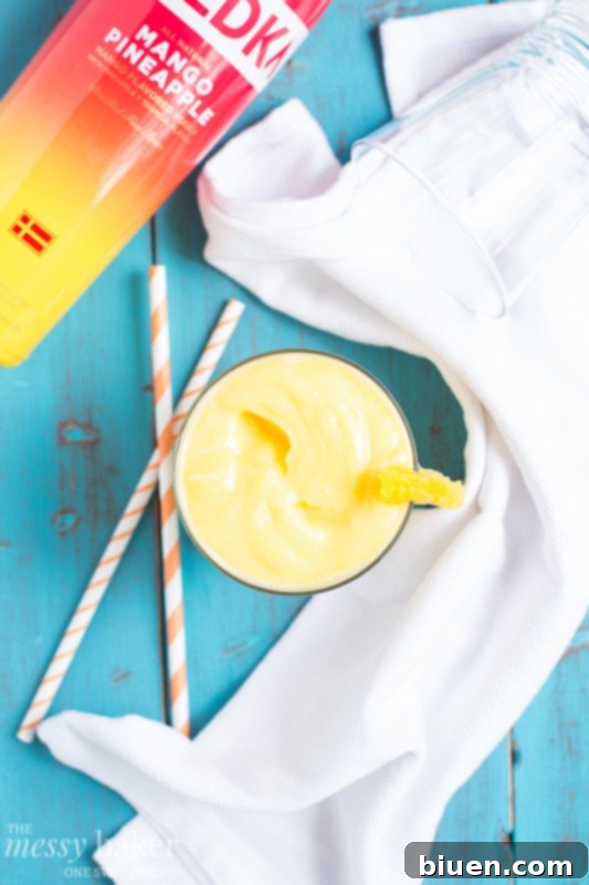 Hand holding a glass of Pineapple Mango Slush Cocktail by the pool