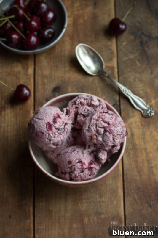 Rich and creamy homemade toasted almond and cherry ice cream in a bowl, topped with fresh cherries and almonds.