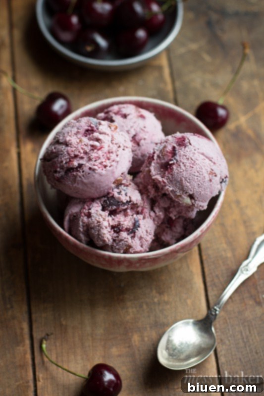 Close-up of a perfectly scooped homemade toasted almond and cherry ice cream, revealing its smooth texture and rich cherry color.