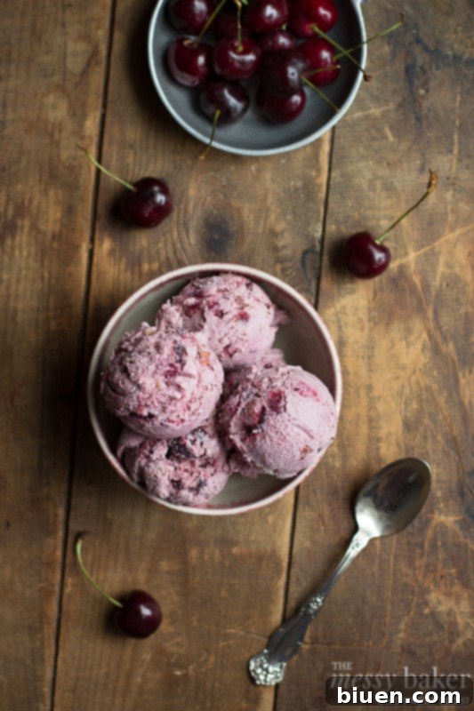 A close-up shot of a scoop of homemade cherry ice cream with visible almond pieces, highlighting its vibrant red color and creamy texture.
