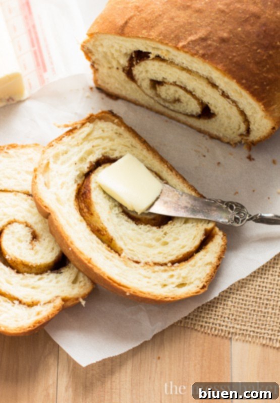 A freshly baked Cinnamon Swirl Loaf, golden brown and glistening, cooling on a wire rack. Perfect homemade sweet bread recipe. | www.themessybakerblog.com