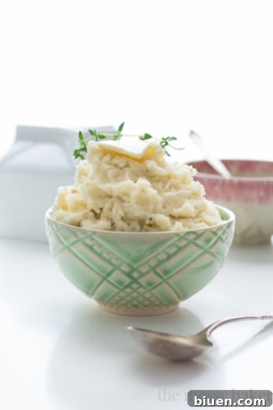 A beautifully presented bowl of smooth mashed potatoes, garnished with fresh herbs and a pat of butter.