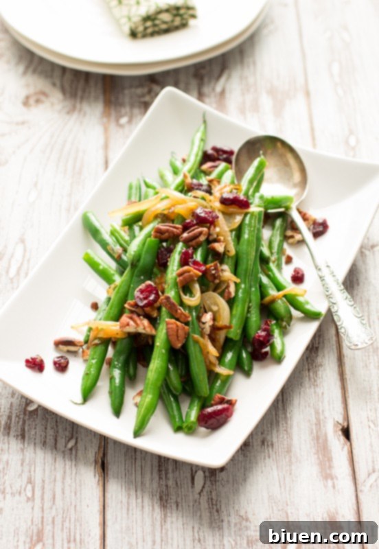 This easy side dish is perfect for Thanksgiving. Crisp green beans get tossed with caramelized onions, toasted pecans, and dried cranberries. | www.themessybakerblog.com