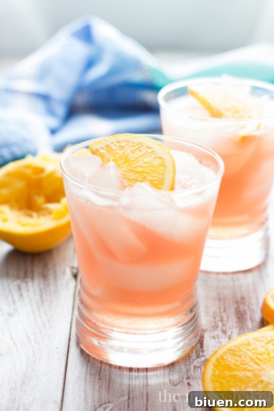 A hand pouring a Cranberry Orange Crush cocktail into a glass filled with ice.
