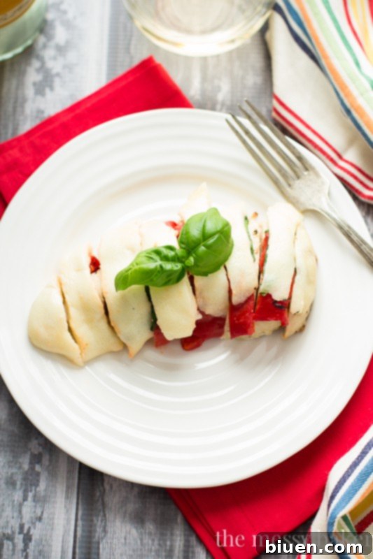 Roasted Red Pepper Caprese Chicken 3 Close-up of baked chicken breast topped with roasted red pepper, fresh basil, and melted mozzarella cheese, garnished with fresh herbs