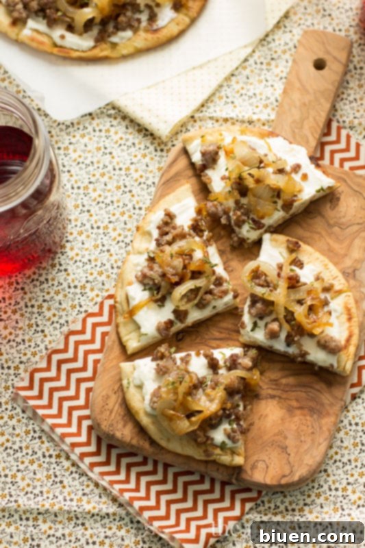 Sausage & Caramelized Onion Pita Pizza slices arranged on a serving board with a wine glass.
