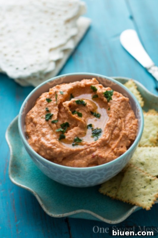 Vibrant Sun-Dried Tomato & Roasted Red Pepper Hummus in a bowl, garnished with herbs.
