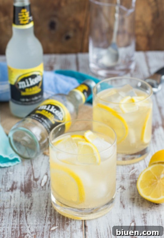 Thirsty Thursday Vanilla Bourbon Quencher 2 A tall glass of Vanilla Bourbon Lemonade garnished with fresh lemon slices and a vanilla bean pod, sitting on a rustic wooden surface with ice.