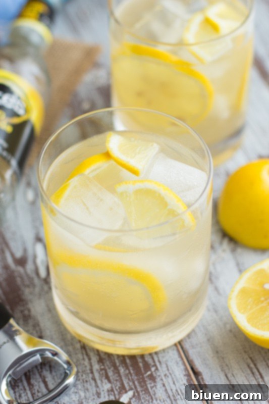 Thirsty Thursday Vanilla Bourbon Quencher 3 Close-up of a hand holding a glass of Vanilla Bourbon Lemonade, with a blurry background suggesting a relaxed outdoor setting.