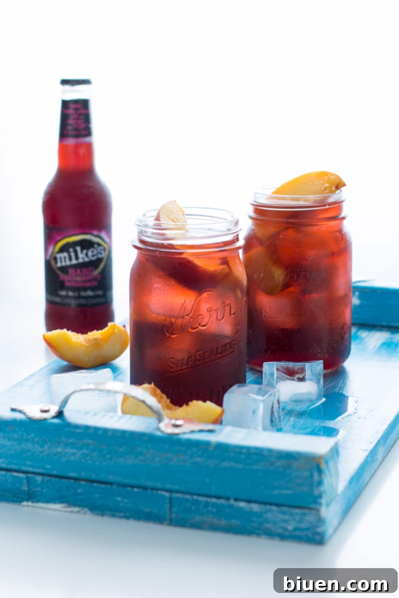 Black Cherry Peach Smash Cocktail - A vibrant, red cocktail with peach slices and ice in a tall glass.