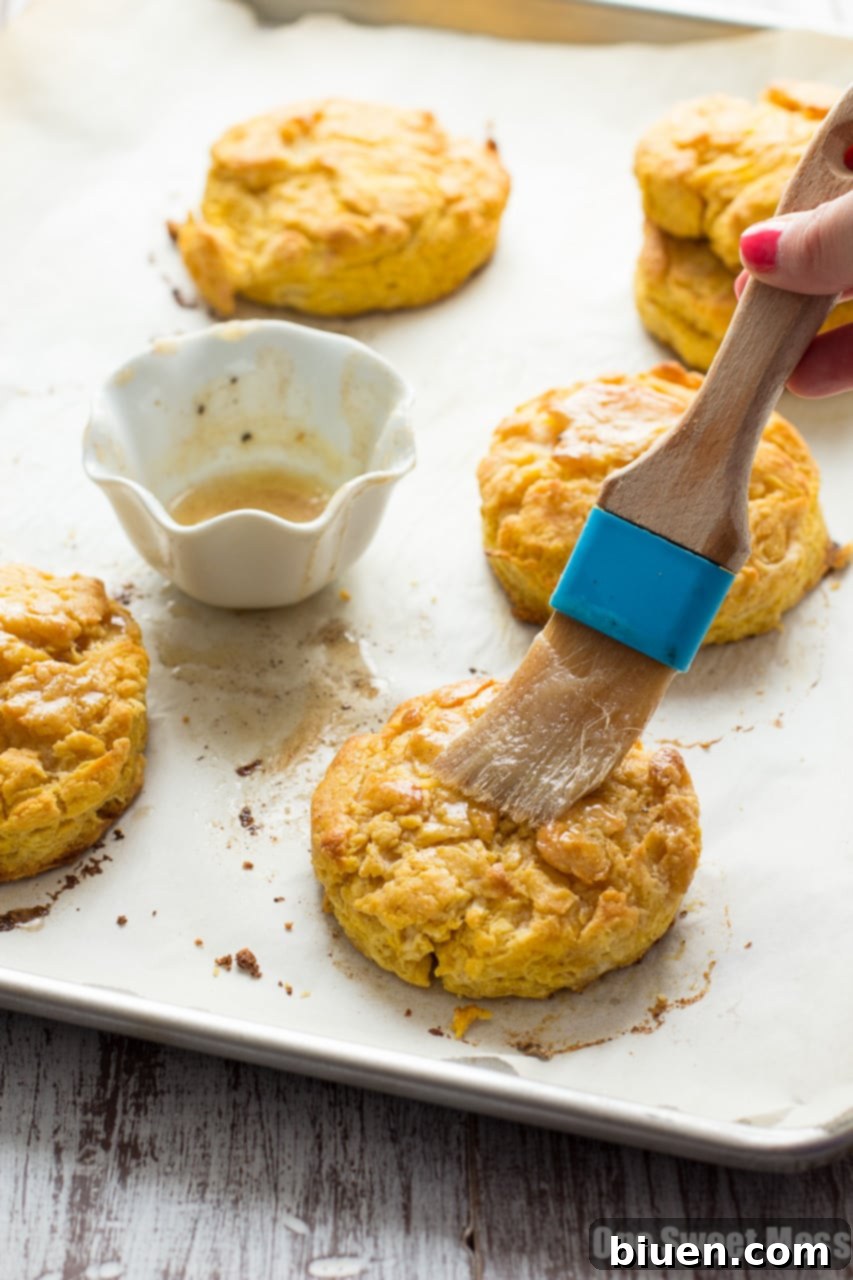 A stack of golden-brown Pumpkin Biscuits, drizzled with glaze, on a white plate